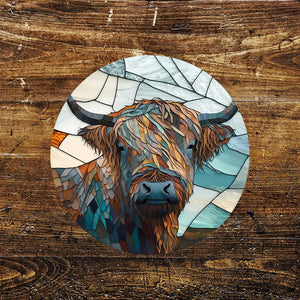 A round metal sign featuring a Highland cow design in a stained glass effect, with earthy tones and frosty hues. The sign is placed against a rustic wooden background, highlighting its unique artistic detail.