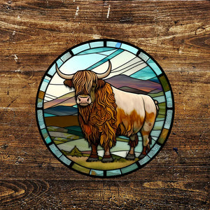 A round metal sign featuring a Highland cow in a scenic countryside setting with a stained glass effect design, framed in a decorative border. The sign is displayed on a rustic wooden background.