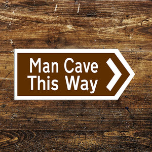 Brown and white “Man Cave This Way” metal sign with an arrow pointing right, mounted on a rustic wooden background. Perfect for home bars, garages, or game rooms.