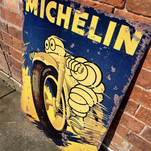 Close-up of the Michelin Motorcycle Tires metal sign, showing distressed edges and retro artwork of the Michelin Man on a speeding motorbike.