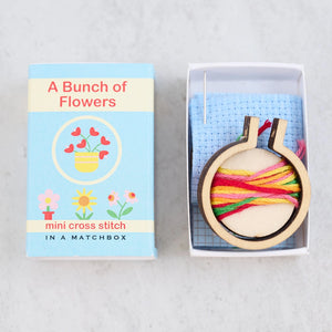 Open matchbox revealing a mini cross stitch kit with embroidery floss and hoop.