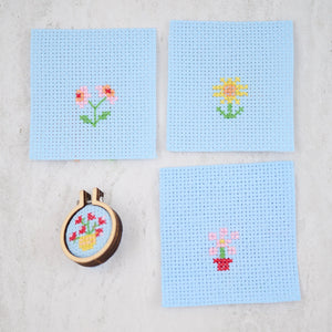 Four finished floral cross stitch designs on Aida fabric with a completed hoop.