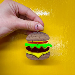 Front view of large handmade burger earring with layered Perspex acrylic and wood design on yellow background.