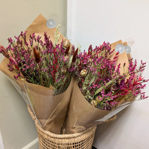 A beautifully arranged Burgundy Dried Flower Arrangement in eco-friendly kraft wrapping, placed in a woven basket.