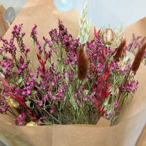 Close-up of dried flowers in deep pink and red tones, featuring wheat stems and natural grasses.