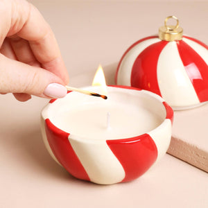 Close-up of Candy Cane Stripe Cinnamon Bauble Candle being lit, showing red and white ceramic design.