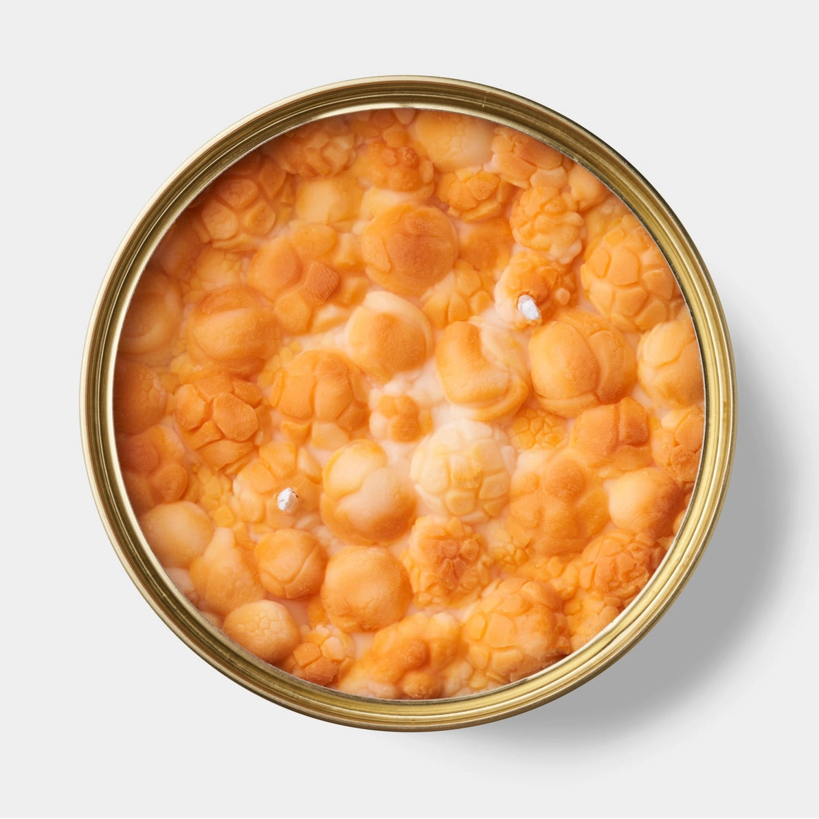 Overhead view of caramel popcorn-shaped candle wax inside a gold tin, featuring two wicks and a hyper-realistic popcorn texture.