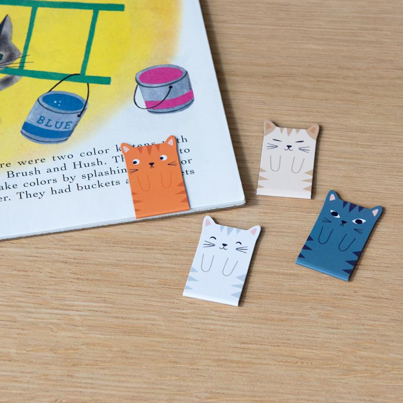 Cat magnetic bookmarks clipped onto open children's book on wooden surface