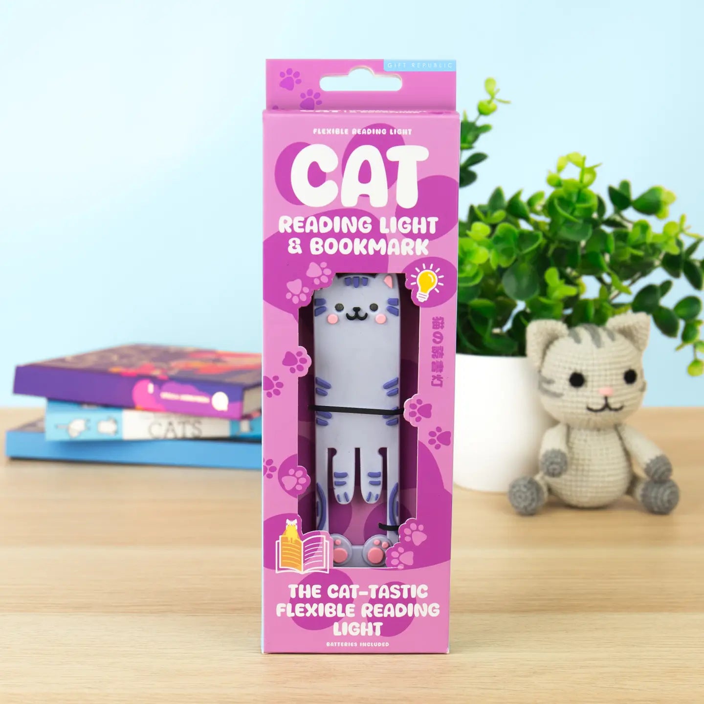 Front view of Cat Reading Light and Bookmark in purple packaging, displayed on a wooden desk with cat-themed books and a plush toy in the background.