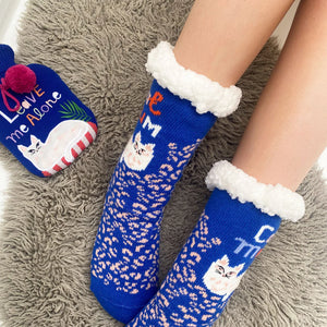 Feet in Catnip Cozy Slipper Socks next to matching mini hot water bottle with cat illustration and “Leave Me Alone” text, styled on a soft grey rug.