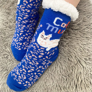 Close-up of Cat Mum slipper socks worn on feet, focusing on the cheeky cat face design and bold blue knit with peach animal print accents.