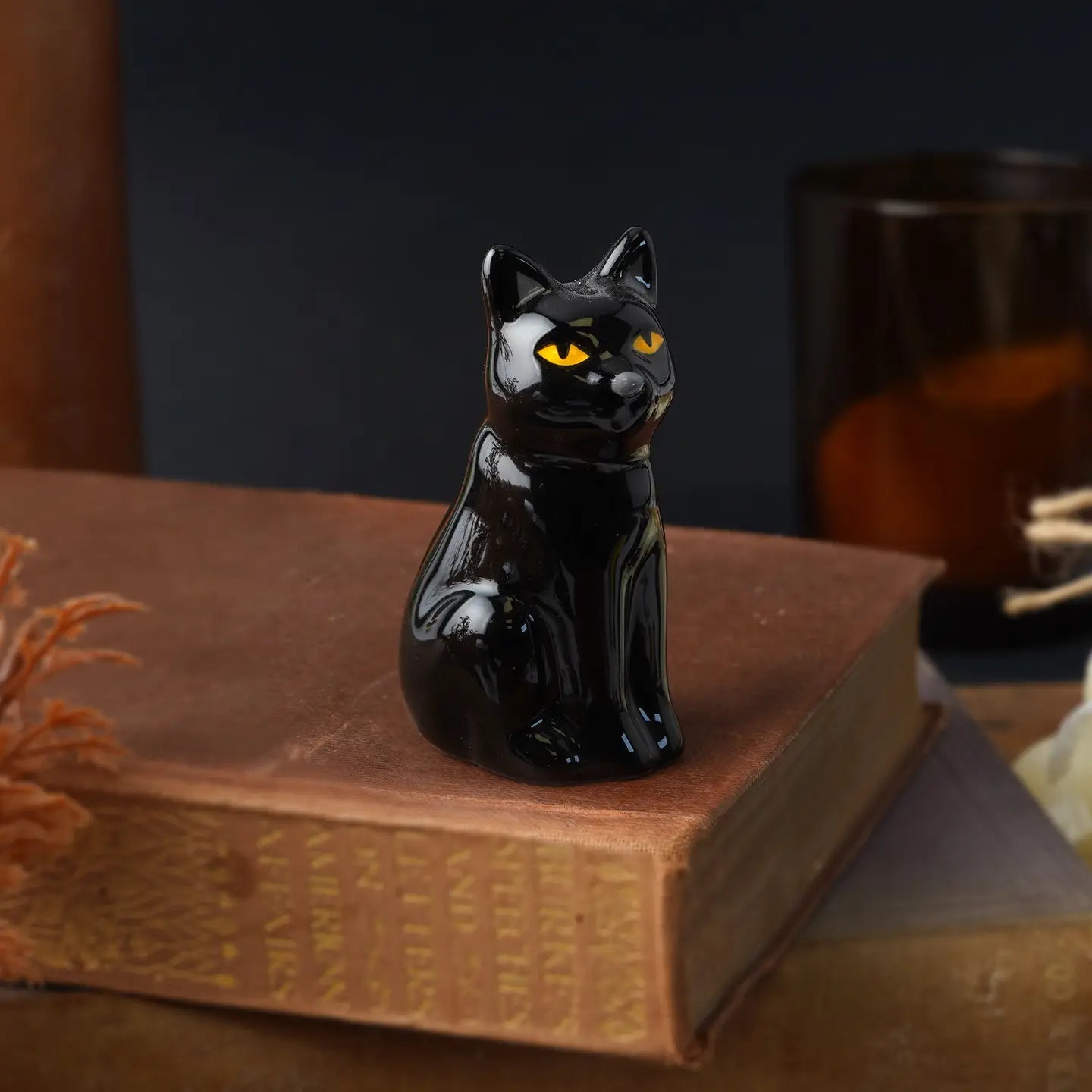 Glossy black ceramic cat figurine with golden eyes on vintage book stack.