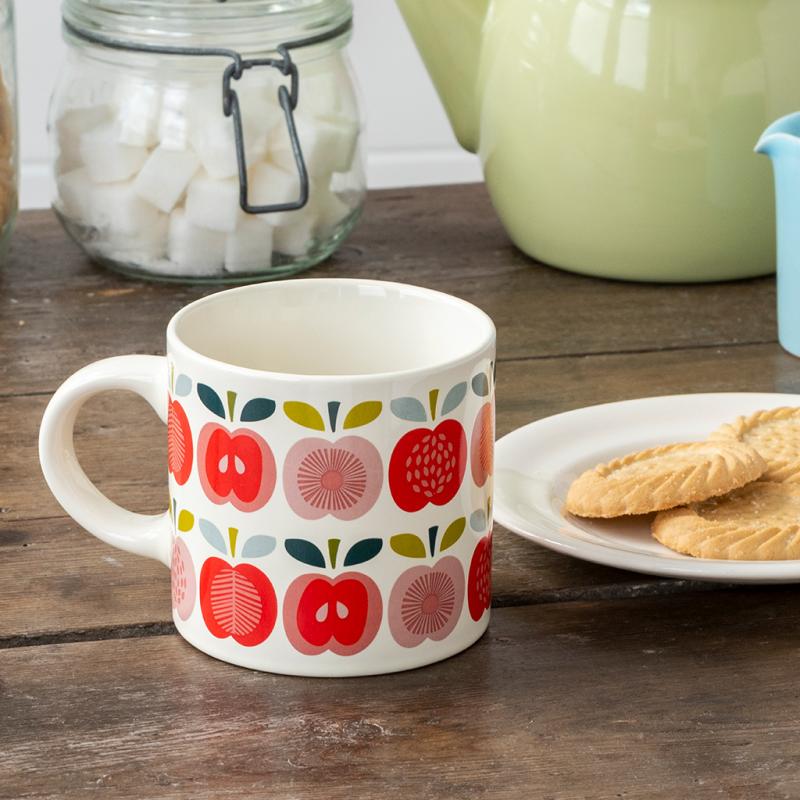 Vintage Apple ceramic mug on a rustic table with biscuits, sugar jar, and green teapot in the background.