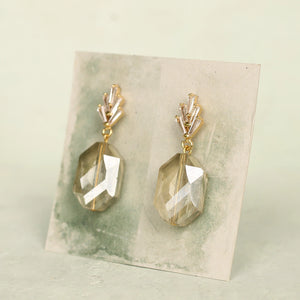 Pair of champagne yellow art deco drop earrings with faceted glass stones and gold-tone fittings displayed on a green and cream backing card