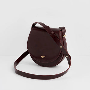 Side angle of Fable England Cherry Red Saddle Bag showcasing structured saddle silhouette and adjustable shoulder strap.