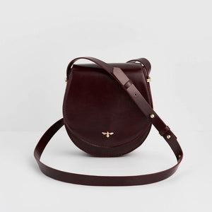 Front view of Fable England Cherry Red Saddle Bag in smooth faux leather with gold bee emblem and adjustable strap.