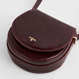 Close-up of Fable England Cherry Red Saddle Bag showing smooth faux leather finish and gold bee clasp detail.
