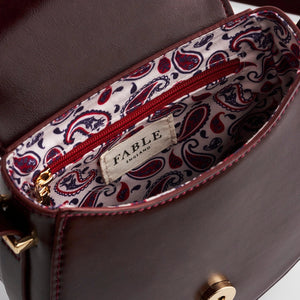 Interior view of Fable England Cherry Red Saddle Bag revealing paisley-print fabric lining and internal zipped pocket.