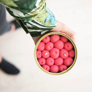 Top-down view of cherry-scented candle being held in hand, showcasing realistic red wax cherries in a tin.