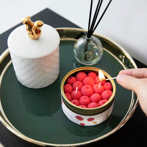 Person lighting cherry-scented candle shaped like cherries on a stylish tray with ceramic and reed diffuser decor.