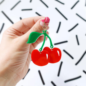 Side view: Close-up of a single cherry earring held in hand against graphic background.