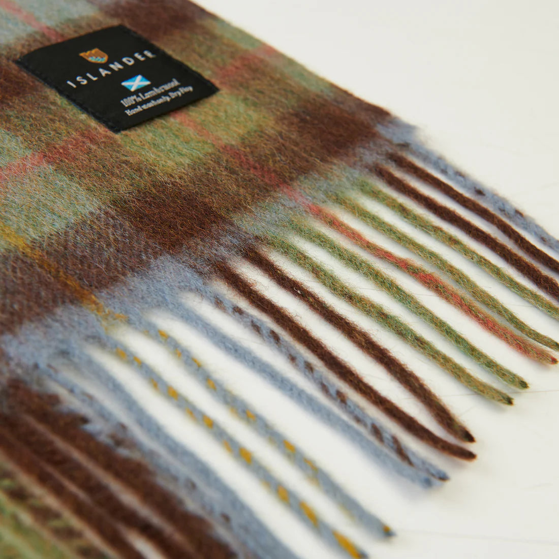 Close-up of chestnut and blue tartan lambswool scarf fringed edge with woven label.