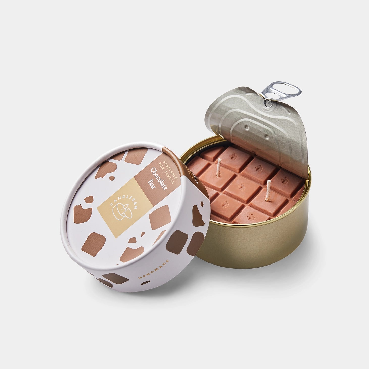 Front view of chocolate bar candle in opened tin, showing realistic chocolate block texture and three wicks, with stylish packaging beside it.
