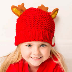 Smiling toddler wearing red Christmas Reindeer Hat with reindeer ears and antlers – cosy festive children’s winter hat.