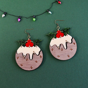 Front view of large Christmas pudding statement earrings with engraved wooden texture, glossy acrylic brandy sauce, red berries, and glitter holly leaves.