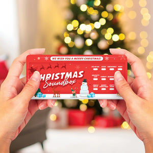 Person holding the red Christmas Soundbox in front of a blurred Christmas tree, showing clearly labelled festive sound buttons like “Reindeer”, “Party Horn”, and “Merry Christmas”.