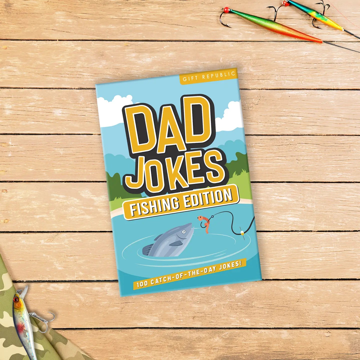 Dad Jokes Fishing Edition deck on a wooden surface with fishing lures – novelty joke card set for anglers.