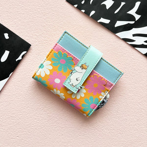 Flat lay of Moomin Flower Fold Over Card Holder with Snorkmaiden design on pastel pink background with floral print and soft blue strap.
