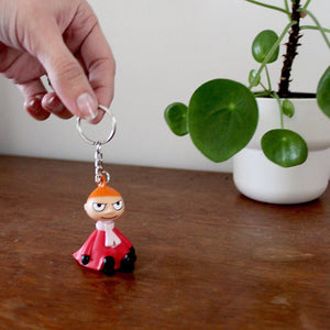 A person holding a Moomin “Little My” light-up keyring above a wooden surface with a green plant in the background.