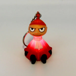 The Moomin “Little My” keyring illuminated, glowing red while resting on a white surface.