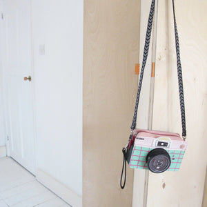 Disaster Designs Pix Camera Mini Bag hanging on a wooden door with its detachable black and white chevron strap.