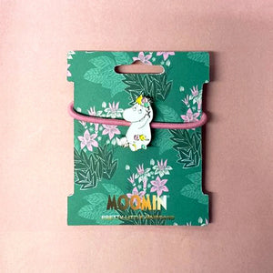 A Disaster Designs Snorkmaiden Enamel Hairband displayed on a green floral-themed packaging card with a pink elastic band.