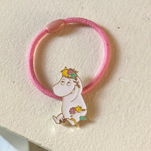 The Snorkmaiden Enamel Hairband placed on a white surface, showing its delicate enamel details and soft pink elastic band.