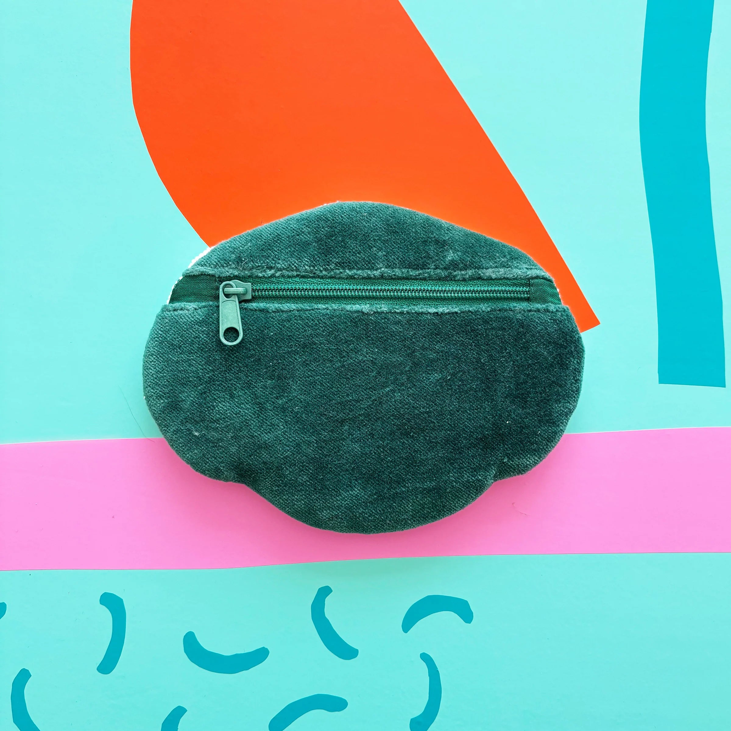 Hand holding beaded Dog House Coin Purse with pink and teal backdrop.