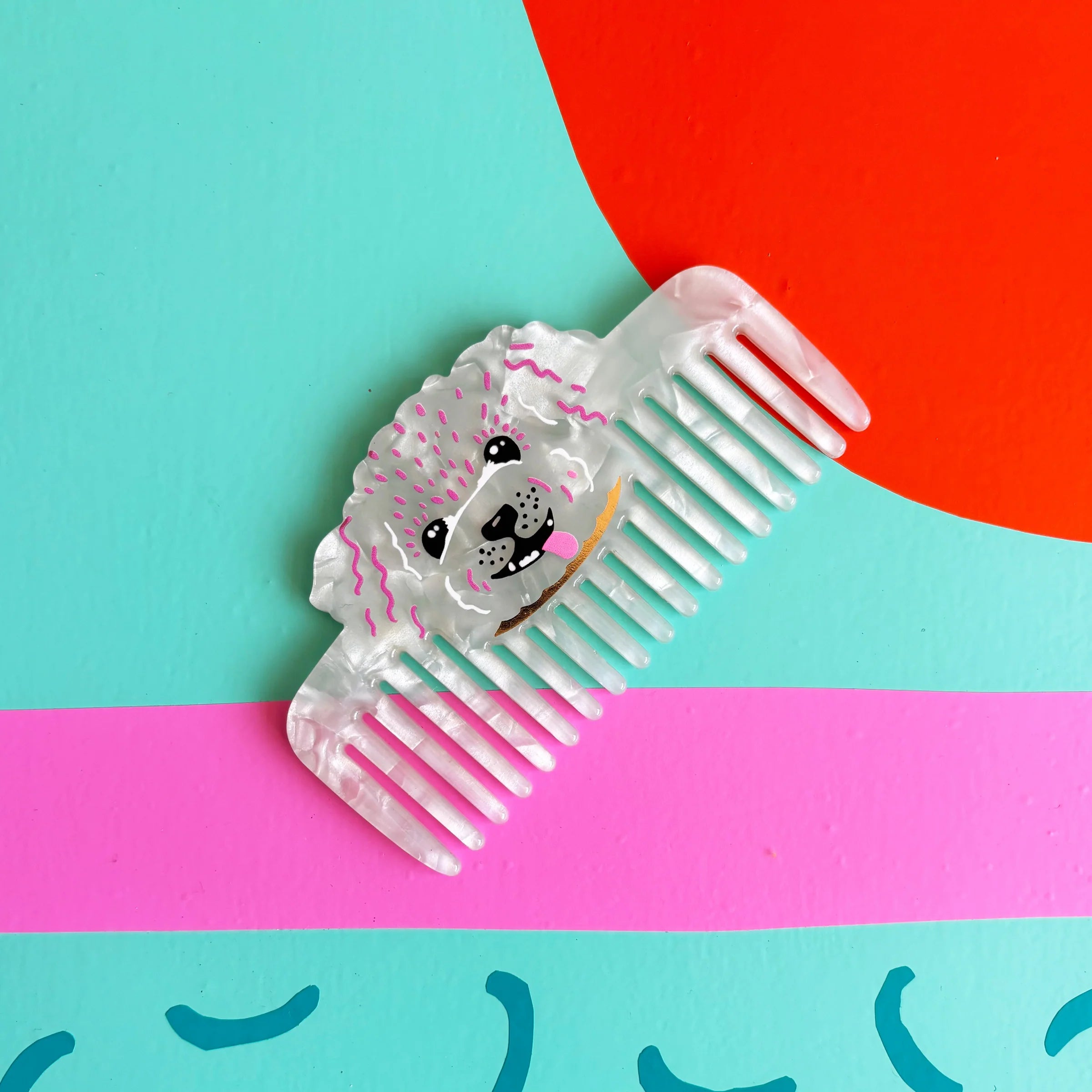 Close-up of pearlescent dog comb on teal and pink background – Dog House Hair of the Dog Comb detail.