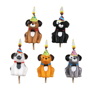 Set of five colourful 3D dog-shaped cake candles with party hats, each with a lit flame, displayed upright on white background.