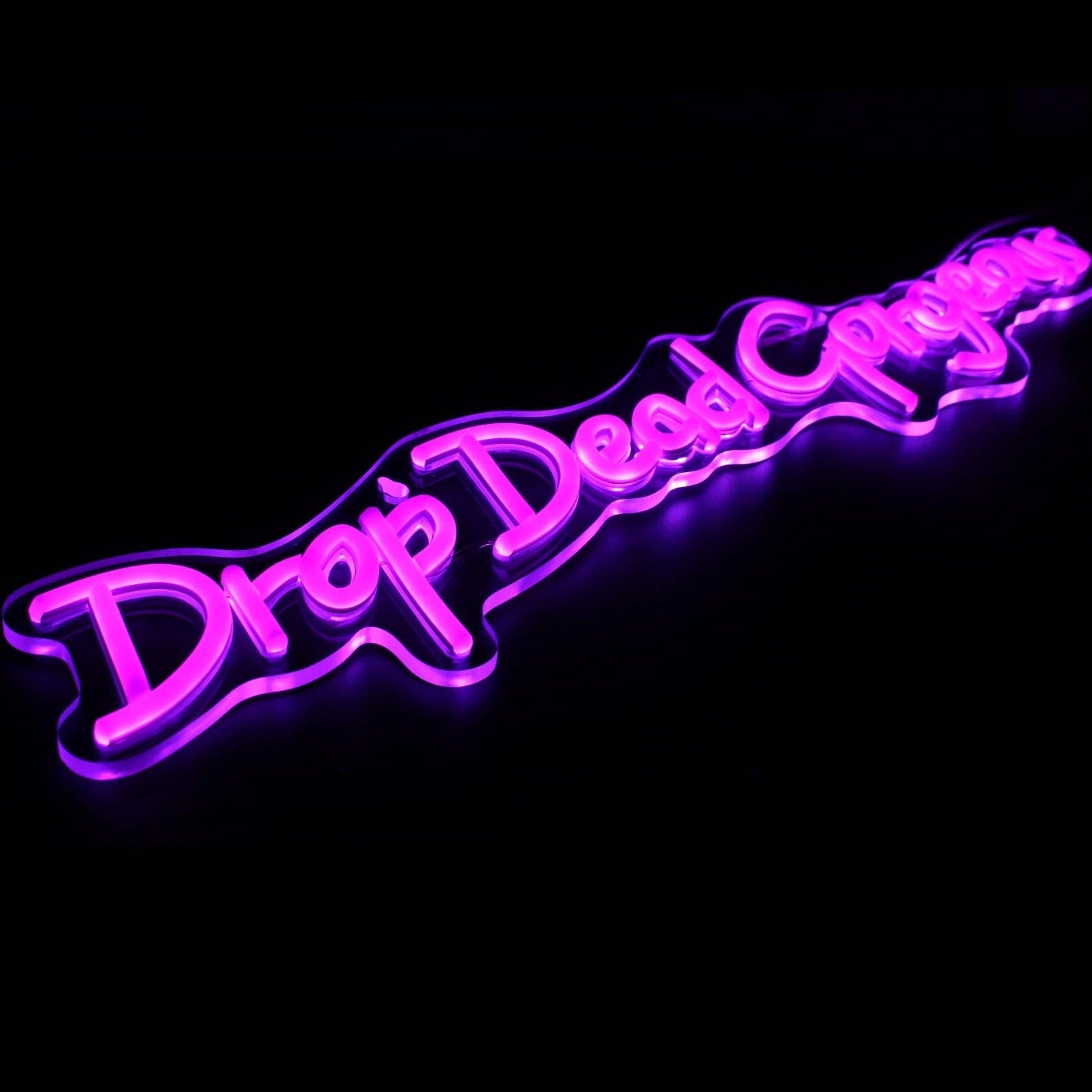 Side angle of Drop Dead Gorgeous pink neon wall sign lit up against a black backdrop.