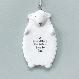 White porcelain sheep-shaped hanging plaque with the phrase “A friendsheep like ours is hard to find”, displayed against a grey background.