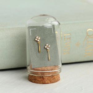 Edwardian gold drop earrings displayed under a glass dome with a vintage book in the background