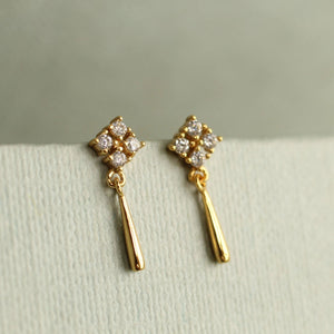 Close-up side view of dainty cubic zirconia gold stud earrings resting on a pale green book edge.