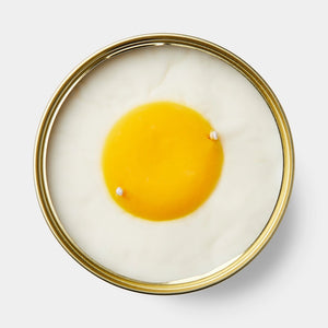 Top-down view of the Vanilla Egg Candle showing a detailed yellow yolk shape and two wicks, crafted from a smooth soy and coconut wax blend.