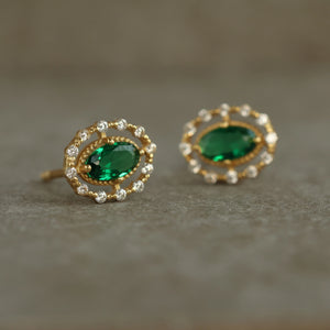 Close-up of Emerald Queen Jewel Stud Earrings on a neutral surface, showcasing the emerald-green centre stone.