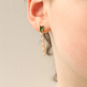 A close-up shot of a person wearing an emerald baguette crystal drop earring. The earring dangles elegantly, showcasing its vintage-inspired rectangular stones.