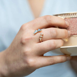Model wearing Enamel Blue Butterfly Ring with gold band and blue butterfly charm while holding a teacup.
