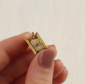 A close-up of a hand holding a tiny brass book locket, opened to reveal miniature folded pages with a hidden message inside.