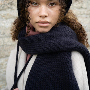 Close-up portrait of woman wearing Fable Forget-Me-Not Knitted Navy Scarf and matching bonnet with floral details.